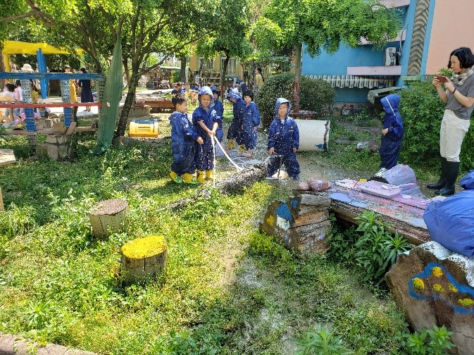 Multiple young children stand with overalls on playing with dirt