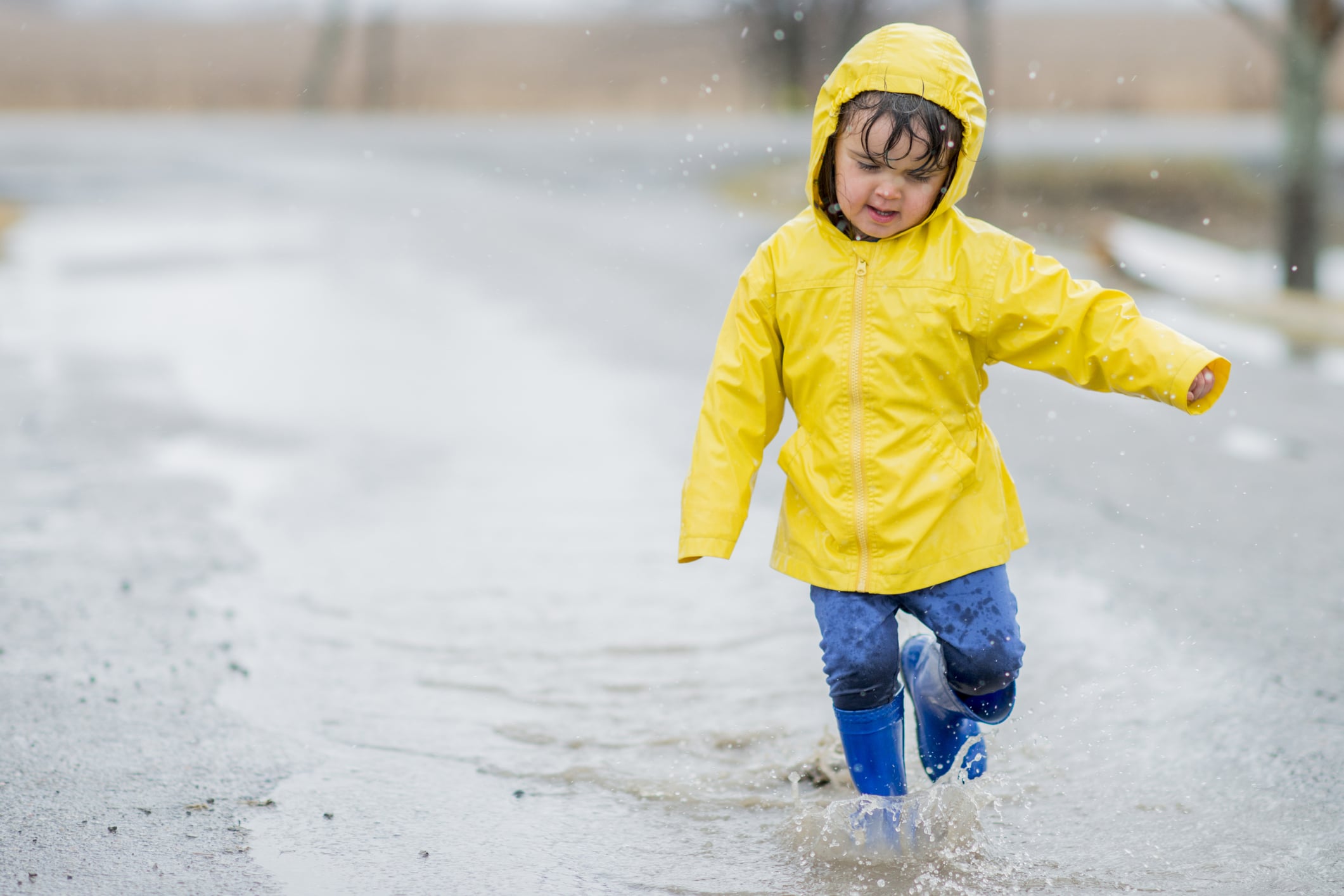 girl in yellow raincoat splashing in puddle