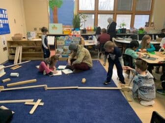 Children and adults scattered around the classroom. They are building, drawing, and talking.