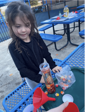 Young child with funnel, clear tube and small, colorful objects.