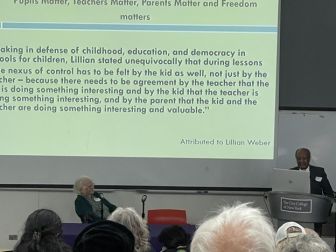 A woman sits next to a lectern while a man presents a slide with a quote attributed to Lillian Weber at The City College of New York.