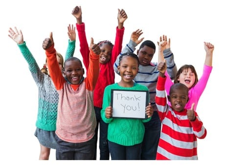 A group of smiling children stand together with raised arms, and one child holds a sign that says
